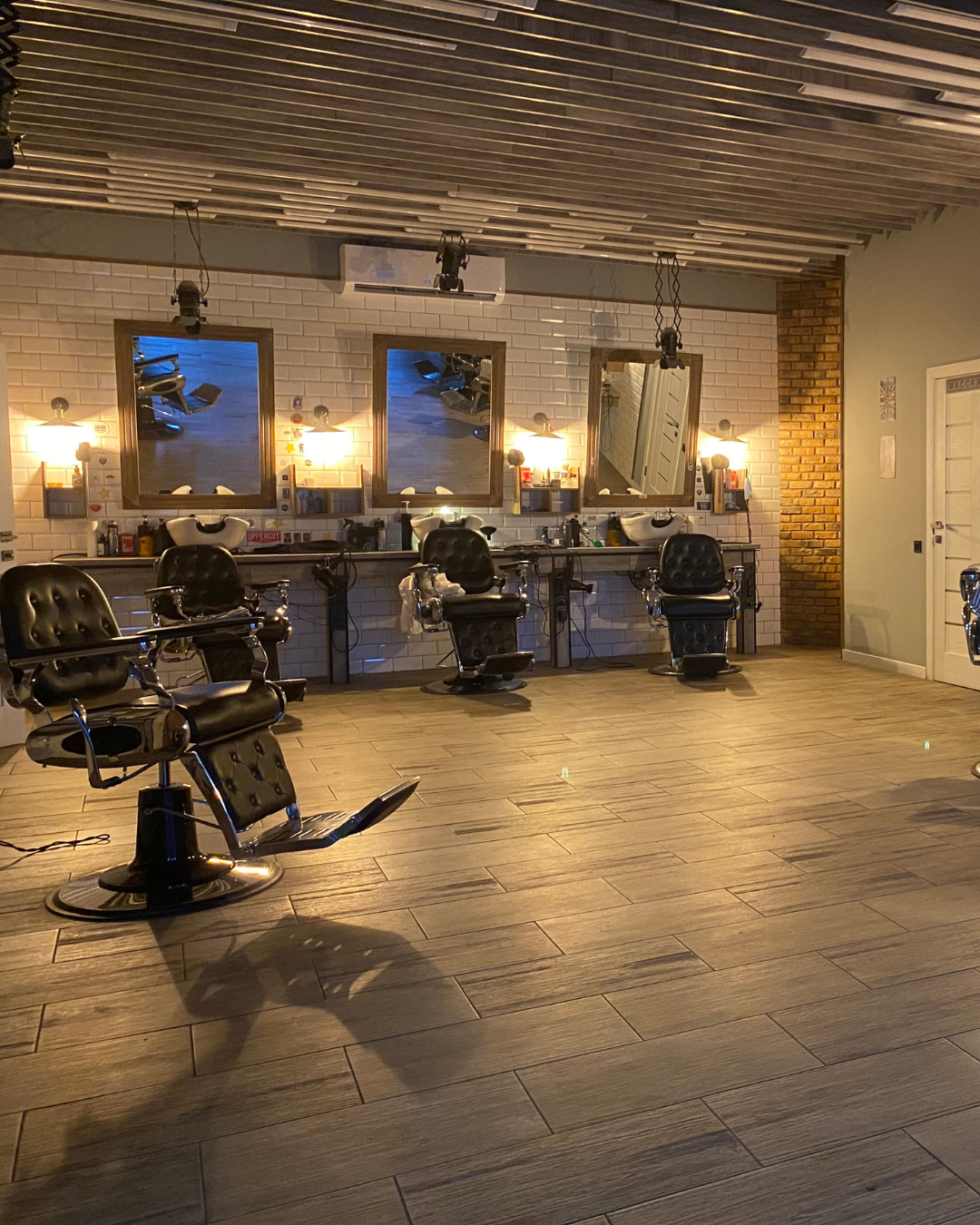 Salão amplo de barbearia com iluminação quente e cadeiras de couro